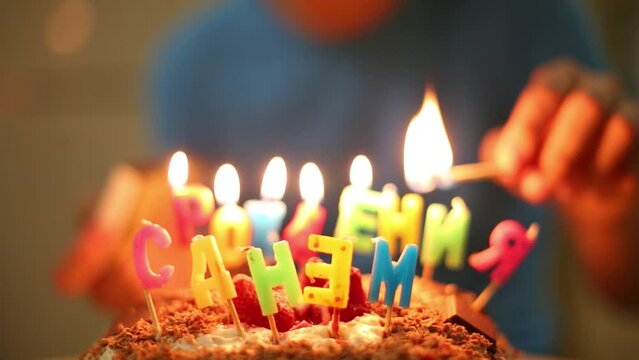 A boy lights candle in form of inscriptions Happy Birthday on the cake