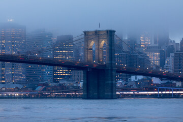 Brooklyn Bridge illuminated at dusk with low clouds