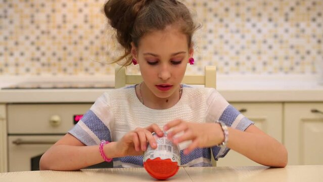 Girl takes off the wrapper from big egg Kinder Surprise in the kitchen