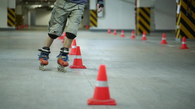 Man circling line of orange cones on roller skates on parking.