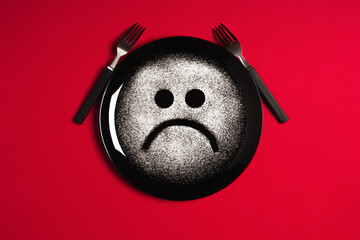 Sad face, concept made with plate and flour, red background, star shaped eyes, black plate, happy mood, facial expressions, forks in the shape of arms with different positions