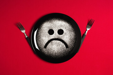 Sad face, concept made with plate and flour, red background, star shaped eyes, black plate, happy mood, facial expressions, forks in the shape of arms with different positions