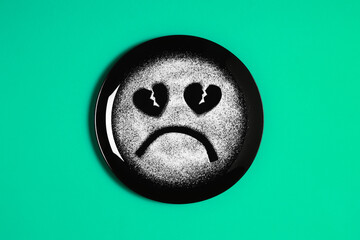 Sad face, face I don't like, concept made with plate and flour, light green background, heart shaped eyes, black plate, sad mood, facial expressions
