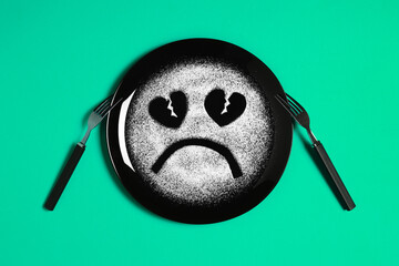 Sad face, face I don't like, concept made with plate and flour, light green background, heart shaped eyes, black plate, sad mood, facial expressions, forks in the shape of arms with different position