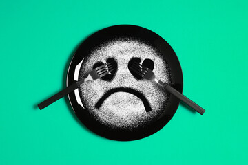 Sad face, face I don't like, concept made with plate and flour, light green background, heart shaped eyes, black plate, sad mood, facial expressions, forks in the shape of arms with different position