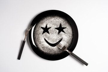 Smiling face, concept made with plate and flour, white background, star shaped eyes, black plate, happy mood, facial expressions, forks in the shape of arms with different positions