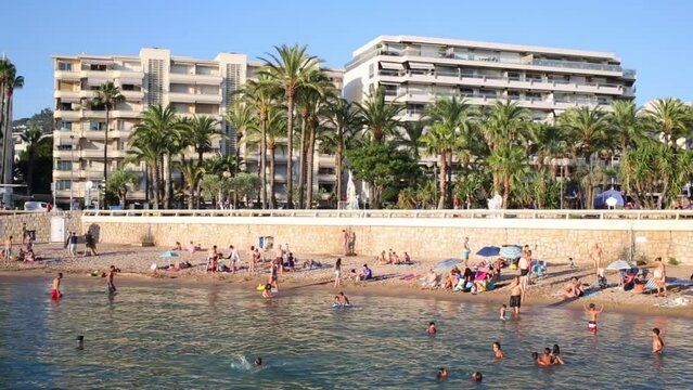 People swim and sunbathe on beach at end of Promenade de la Croisette