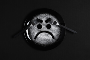 Displeased face, frowning eyebrows, concept made with plate and flour, black background, black plate, facial expressions, forks in the shape of arms with different positions