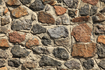 Granite wall, background. Surface of stone structure built of granite rocks (bricks). The wall texture of volcanic yellow and brown color. Fence with large stones on cement base in the rays of the sun