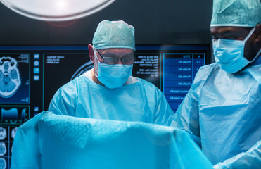 Team of medical doctors performs surgical operation in modern operating room using high-tech...