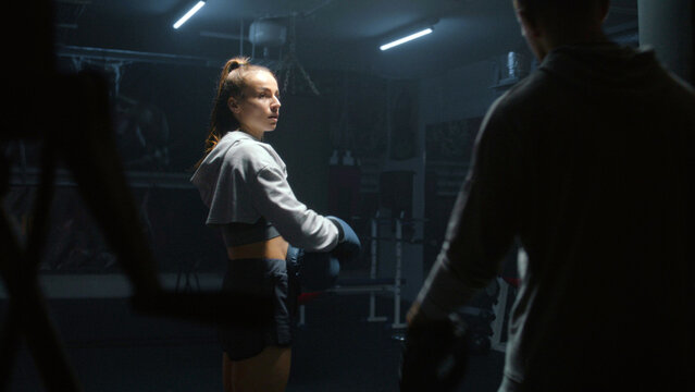 Athletic fighter in boxing gloves trains and exercises for fighting championship. Woman hits punching mitts and practices in fighting techniques with adult trainer. Physical activity and workout.
