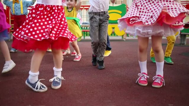 Legs of fourteen girls and boys energetic dancing twist on red playground.