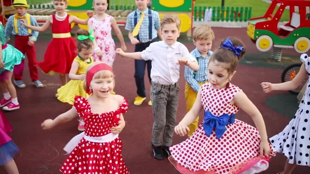 Fourteen small girls and boys raising arms and dancing twist