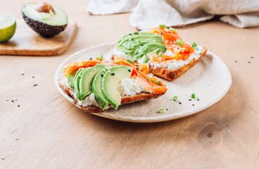 Healthy breakfast sandwiche with salmon, cream cheese and avocado on wooden table.