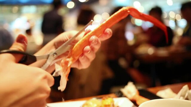 Hand with scissors trying to cutting orange leg of crab close up.