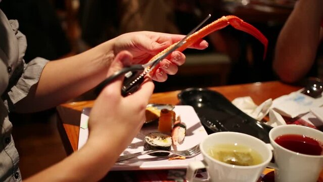 Woman hand trying to break long leg of crab and taking special scissors