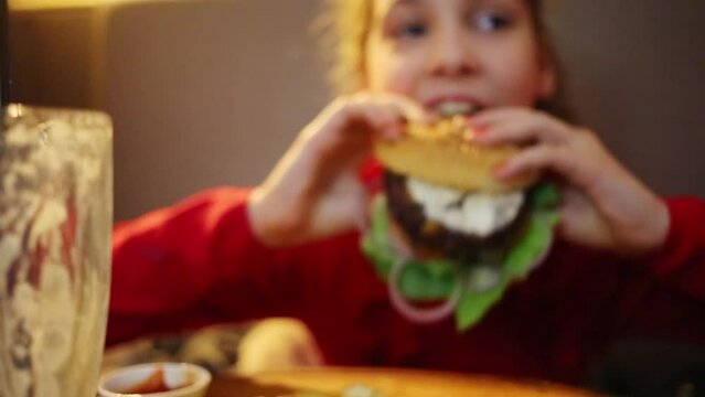 Happy girl eats big appetizing hamburger in restaurant