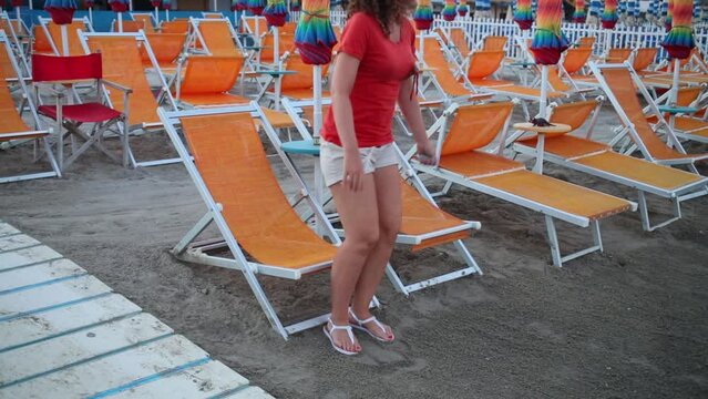 Woman rises from one of the sun loungers on a empty beach at twilight