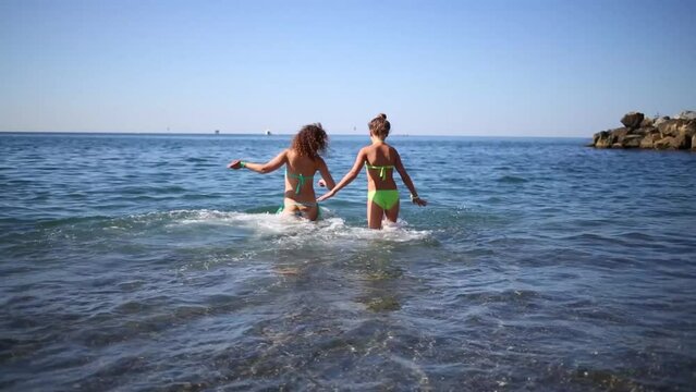 Mother and daughter in bathing suits run into the sea and start splashing