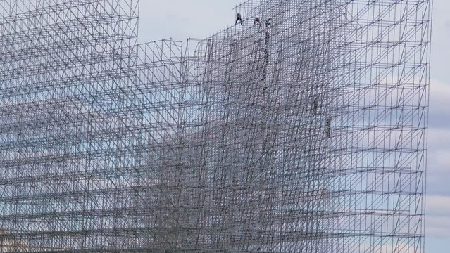 People work on large scaffold and pass by chain something at construction site