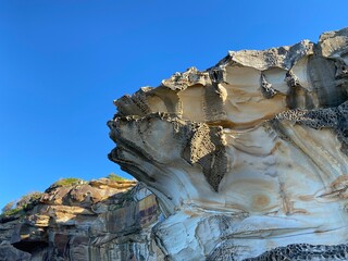Rock formation under a blue sky. White and brown rock undulating in the sun. Cliff, mineral kingdom on the coast. Wind-sculpted ore. Coastal landscape. Canyon geology. - Powered by Adobe