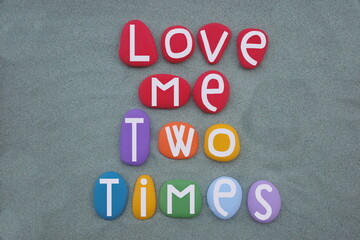 Love me two times, creative message composed with hand painted multi colored stone letters over green sand