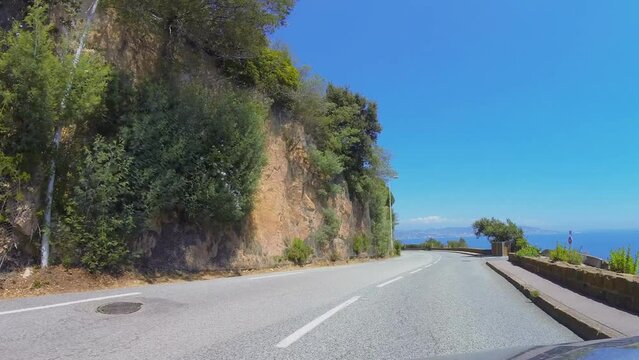 Car rides by mountain road near sea at summer sunny day.