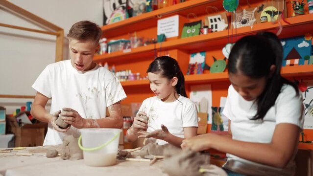 Happy Diverse High School Student Modeling Clay At Pottery Workshop. Cute Children With Mixed Raced Working And Making Cup Of Clay By Using Carving Equipment At Art Lesson. Creative Class. Edification