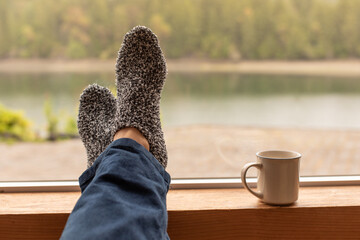 Person at home relaxing with feet up by the window enjoying a morning cup of coffee 