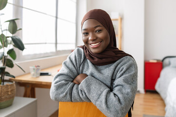 Portrait of young african girl smiling at camera while relaxing on her room. Proud people and...