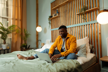 Young African American man hipster copywriter wearing colorful clothes sitting on comfortable bed