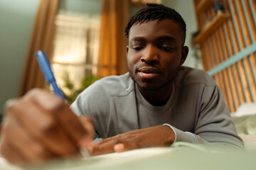 Portrait of serious pensive young attractive African American man, student, taking notes at home