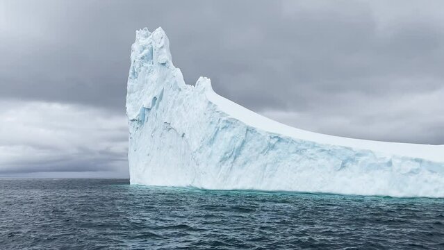 A huge high breakaway glacier drifts in the southern ocean off the coast of Antarctica at sunset, the Antarctic Peninsula, the Southern Arctic Circle, azure water, cloudy weather