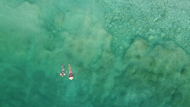 Woman and daughter are swimming in crystal clear sea water. Drone, aerial view.