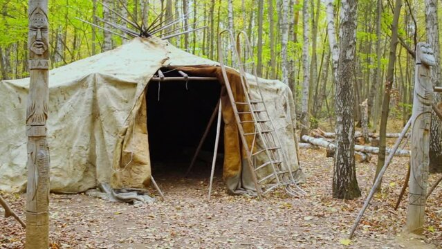 Totem pillar and fells are near wigwam among trees at autumn day