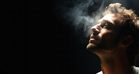 Portrait of a young man smoking cigarette on dark background. Copy space.