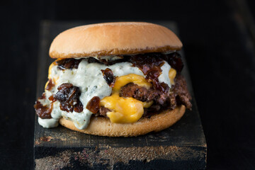 fast food, burger, brioche bun, cheddar cheese, red meat and caramelized onion with mayonnaise, dark background, rustic wood, front photo