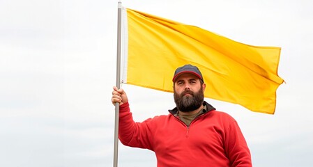 Bearded man in red sweater and cap with yellow flag on cloudy sky background
