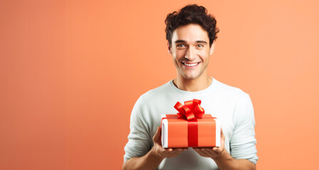 Portrait of a happy young man holding gift box on orange background