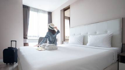 Rear view of tourist woman sitting on bed after arrival at hotel.