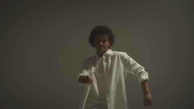 Young inspired man wearing white outfit dancing hip hop barefoot on cyc wall during performance in studio