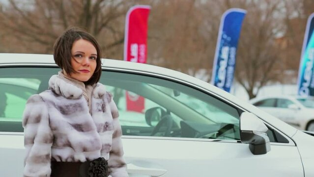 Woman in fur coat closes door of white car at winter day