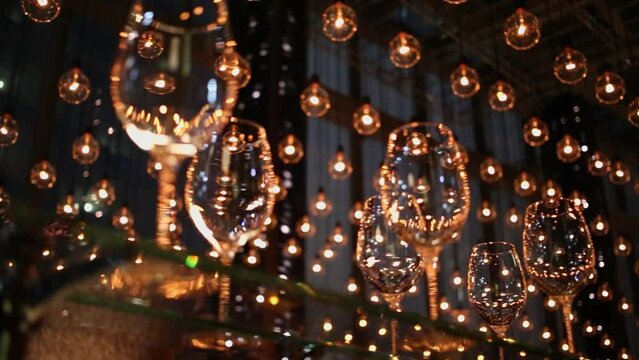 Lot of lighting lamps above vine glasses which stand on glass shelve