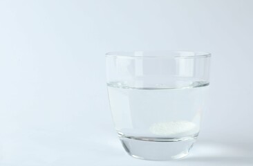 Glass of water with effervescent tablet on white background, space for text