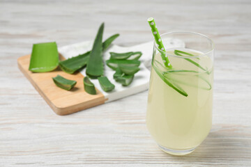 Tasty aloe juice in glass and cut fresh leaves on light wooden table