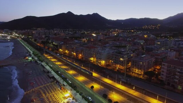 Loano, Italy, Train moves near sea beach and city at summer evening. Aerial view