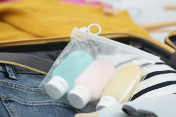 Plastic bag of cosmetic travel kit and clothes in suitcase. Bath accessories