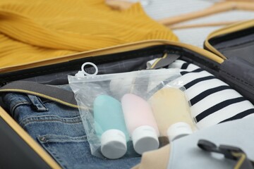 Plastic bag of cosmetic travel kit and clothes in suitcase. Bath accessories