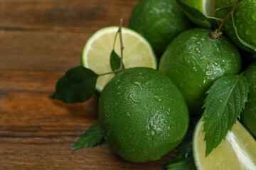 Fresh wet limes and leaves on wooden table, closeup. Space for text