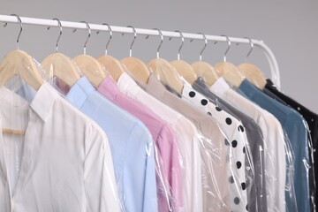 Dry-cleaning service. Many different clothes in plastic bags hanging on rack against grey background